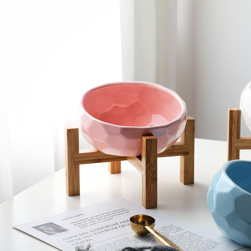 Pink ceramic tilted cat bowl on bamboo stand near window light